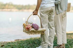 Pareja caminando en jardín con picnic cesta. en amor Pareja es disfrutando picnic hora en parque al aire libre foto