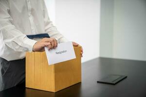 Business man sending resignation letter and packing Stuff Resign Depress or carrying business cardboard box by desk in office. Change of job or fired from company photo