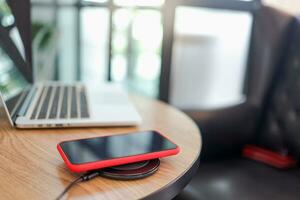 Charging mobile phone battery with wireless device in the table. Smartphone charging on a charging pad. Mobile phone near wireless charger. photo