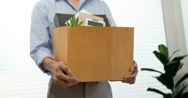 Business man sending resignation letter and packing Stuff Resign Depress or carrying business cardboard box by desk in office. Change of job or fired from company photo