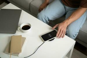 Charging mobile phone battery with wireless charging device in the table. Smartphone charging on a charging pad. Mobile phone near wireless charger Modern lifestyle technology concept. photo