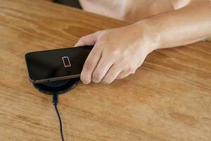 Charging mobile phone battery with wireless charging device in the table. Smartphone charging on a charging pad. Mobile phone near wireless charger Modern lifestyle technology concept. photo