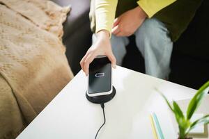 Charging mobile phone battery with wireless charging device in the table. Smartphone charging on a charging pad. Mobile phone near wireless charger Modern lifestyle technology concept. photo