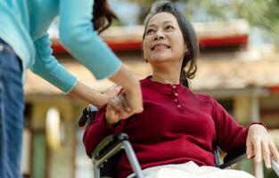 Family relationship Asian senior woman in wheelchair with happy daughter holding caregiver for a hand while spending time together photo