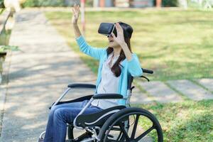 Young asian woman in wheelchair wearing virtual reality touching air during the VR experience. photo