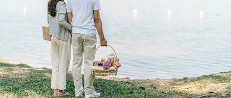 Pareja caminando en jardín con picnic cesta. en amor Pareja es disfrutando picnic hora en parque al aire libre foto