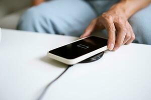 Charging mobile phone battery with wireless charging device in the table. Smartphone charging on a charging pad. Mobile phone near wireless charger Modern lifestyle technology concept. photo