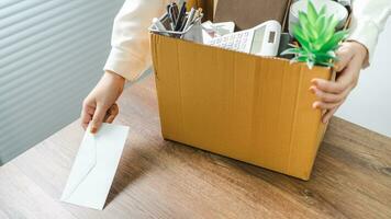 Business woman sending resignation letter and packing Stuff Resign Depress or carrying business cardboard box by desk in office. Change of job or fired from company photo