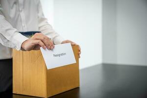 Business man sending resignation letter and packing Stuff Resign Depress or carrying business cardboard box by desk in office. Change of job or fired from company photo