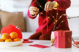 asiático mujer decorado casa para chino nuevo año celebraciones poniendo tradicional colgante a el chino lunar nuevo año para bueno suerte. chino palabra medio bendición foto