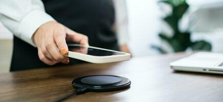 Charging mobile phone battery with wireless charging device in the table. Smartphone charging on a charging pad. Mobile phone near wireless charger Modern lifestyle technology concept. photo