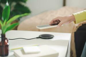 Charging mobile phone battery with wireless charging device in the table. Smartphone charging on a charging pad. Mobile phone near wireless charger Modern lifestyle technology concept. photo