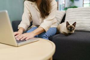 mujer trabajando desde hogar con gato. gato dormido en el ordenador portátil teclado. asistente gato trabajando a ordenador portátil foto