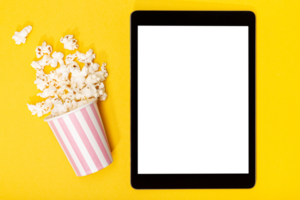 Blank transparent screen tablet and popcorn bucket on yellow background. Template mockup. Top view png