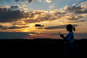 silhouette of woman controlling  drone on sunset background photo