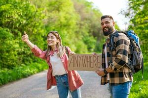 Happy couple hitchhiking on roadside trying to stop car. They are holding cardboard with inscription. photo