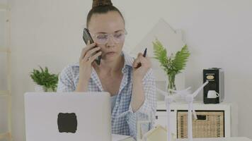 a woman in glasses talking on the phone while sitting at a desk video