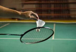 Badminton player holds racket and white cream shuttlecock in front of the net before serving it to another side of the court photo