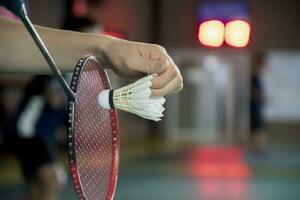 Badminton player holds racket and white cream shuttlecock in front of the net before serving it to another side of the court photo