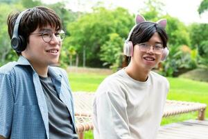 young asian adult couple wearing headphones, sitting, listening to music and spending free time together in front of their house, good relationship and best friends concept. photo