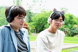 young asian adult couple wearing headphones, sitting, listening to music and spending free time together in front of their house, good relationship and best friends concept. photo