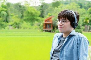 Portrait of young asian adult man wearing headphones, standing, listening to music and spending free time in front of his house, good feeling, loneliness and good time concept. photo