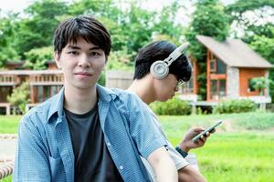 young asian adult couple wearing headphones, sitting, listening to music and spending free time together in front of their house, good relationship and best friends concept. photo