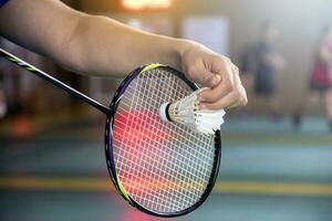 Badminton player holds racket and white cream shuttlecock in front of the net before serving it to another side of the court photo