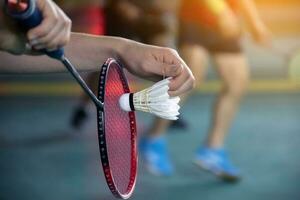 Badminton player holds racket and white cream shuttlecock in front of the net before serving it to another side of the court photo