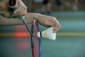 Badminton player holds racket and white cream shuttlecock in front of the net before serving it to another side of the court photo