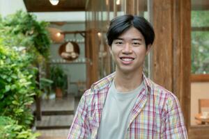 Portrait of asian young adult businessman standing in front of his own coffee shop which located in rural area, soft and selective focus. photo