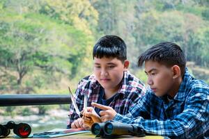 Asian boys are using binoculars to do the birds' watching in tropical forest during summer camp, idea for learning creatures and wildlife animals and insects outside the classroom. photo