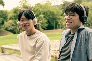 young asian adult couple wearing headphones, sitting, listening to music and spending free time together in front of their house, good relationship and best friends concept. photo