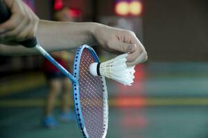 Badminton player holds racket and white cream shuttlecock in front of the net before serving it to another side of the court photo