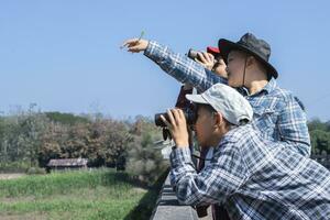 Asian boys are using binoculars to do the birds' watching in tropical forest during summer camp, idea for learning creatures and wildlife animals and insects outside the classroom. photo