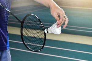 Badminton player holds racket and white cream shuttlecock in front of the net before serving it to another side of the court photo