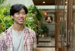 Portrait of asian young adult businessman standing in front of his own coffee shop which located in rural area, soft and selective focus. photo