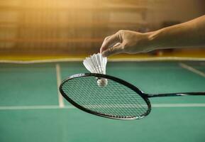 Badminton player holds racket and white cream shuttlecock in front of the net before serving it to another side of the court photo