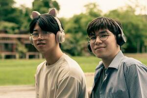 young asian adult couple wearing headphones, sitting, listening to music and spending free time together in front of their house, good relationship and best friends concept. photo