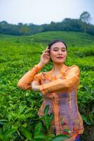 a Javanese woman on vacation in a tea garden wearing a yellow dress photo