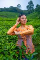 a Javanese woman on vacation in a tea garden wearing a yellow dress photo