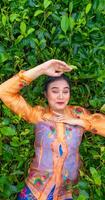 un indonesio mujer es acostado en un verde té jardín mientras en vacaciones foto