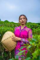 un indonesio mujer en un rosado vestir participación un bambú sombrero en su manos foto