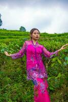 an Asian woman in a pink dress is standing in front of a tea garden photo