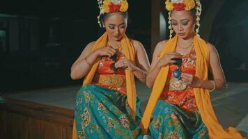 un Pareja de indonesio tradicional bailarines en naranja disfraces son sentado con su amigos en el pabellón video