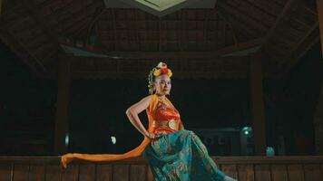 an Asian dancer sitting elegantly in a pavilion wearing an orange costume and scarf video