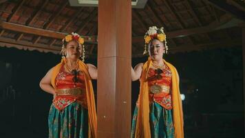 Two traditional Javanese dancers are standing between the pillars of a brown pavilion while wearing Javanese traditional clothes video