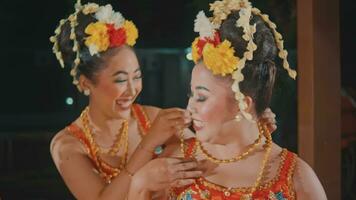 a group of Javanese dancers attaching costume accessories to their friends while getting ready before the stage video