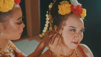 a group of Javanese dancers attaching costume accessories to their friends while getting ready before the stage video