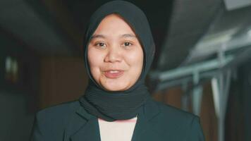 a muslim reporter in a headscarf and a black coat is talking in front of the camera with a smiling face video